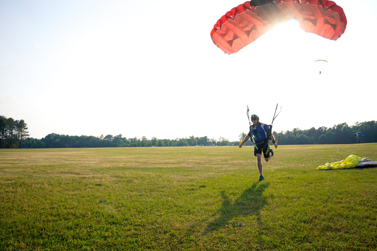 A licensed skydiver touching down with one foot under a red and black canopy. 