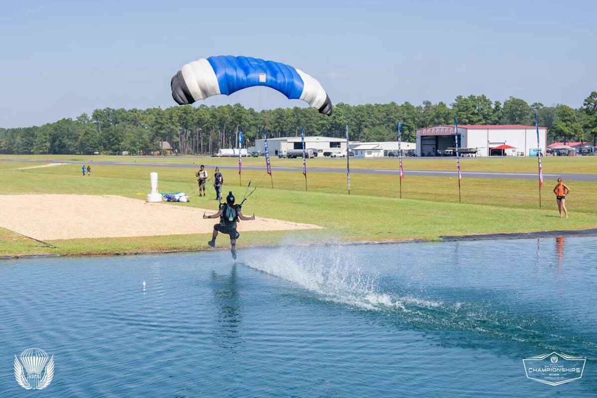 Skydiver swooping and dragging a foot on the water with a blue and white canopy