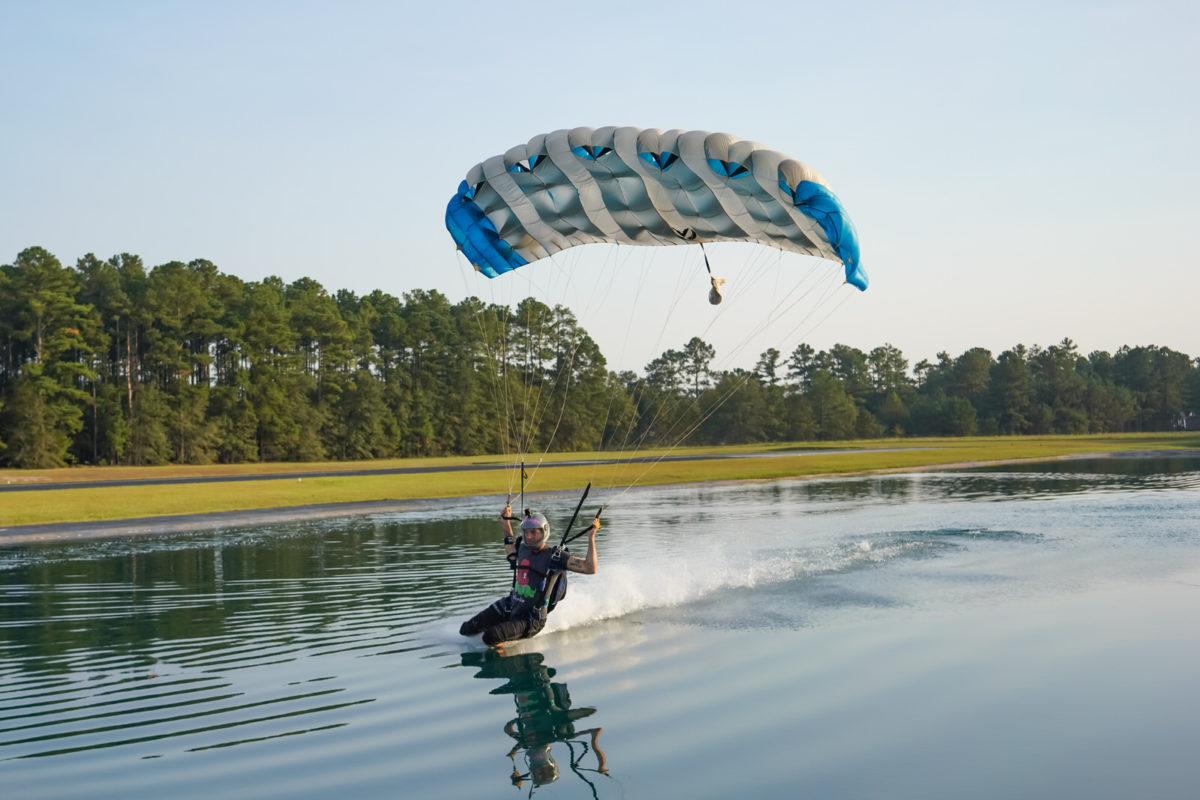 Skydiver swooping their high-performance canopy across a pond of water 