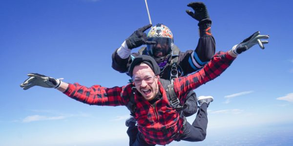 Male tandem student in red and black plaid shirt attached to a tandem instructor in freefall.