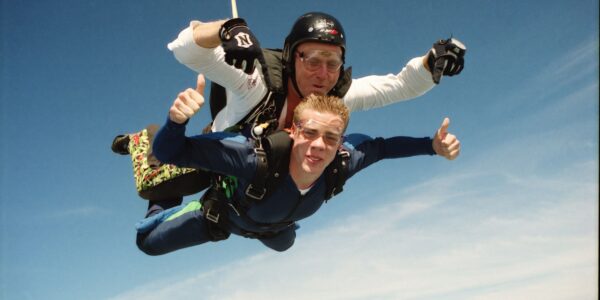 Male tandem student and instructor give a thumbs up during freefall.
