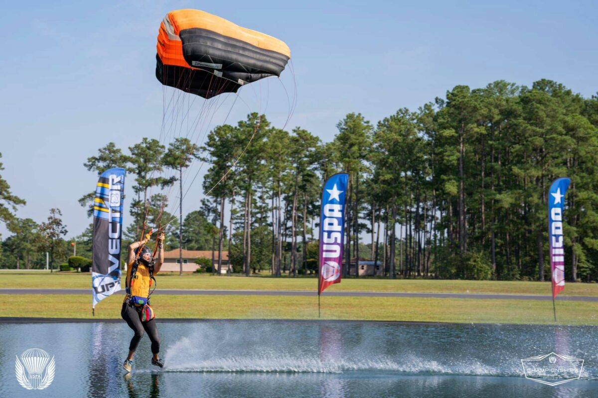 Skydiver drags their feet along a pond while flying their canopy.