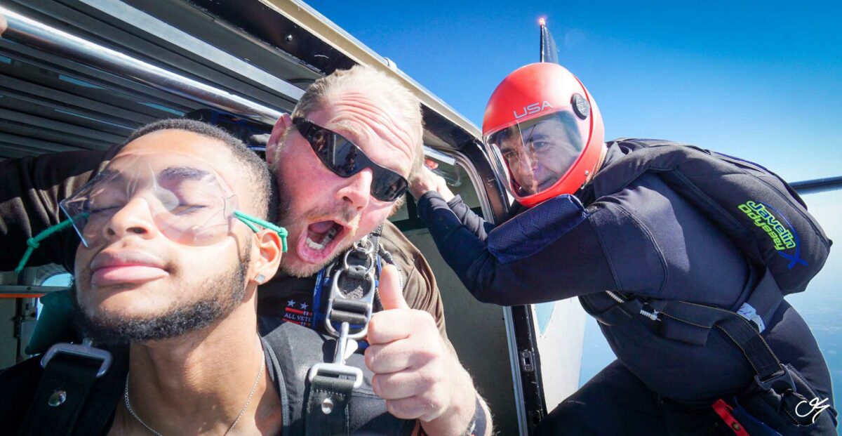 Tandem skydiver with his instructor and videographer prepare to exit the airplane.