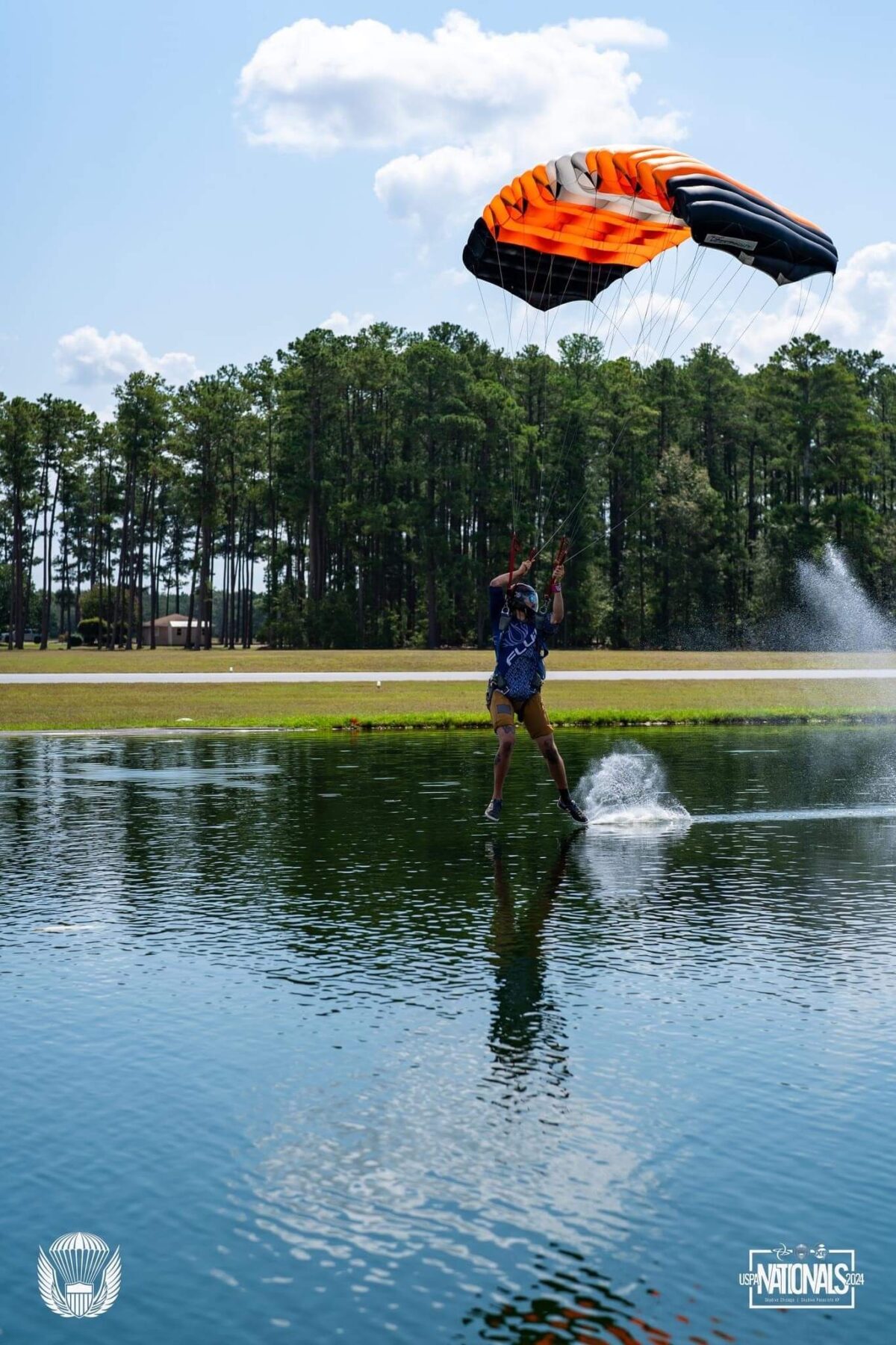 Skydiver skims over pond of water with parachute 