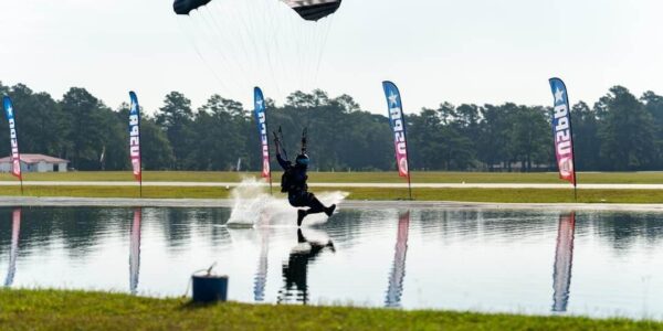 skydiver with parachute gliding over pond of water